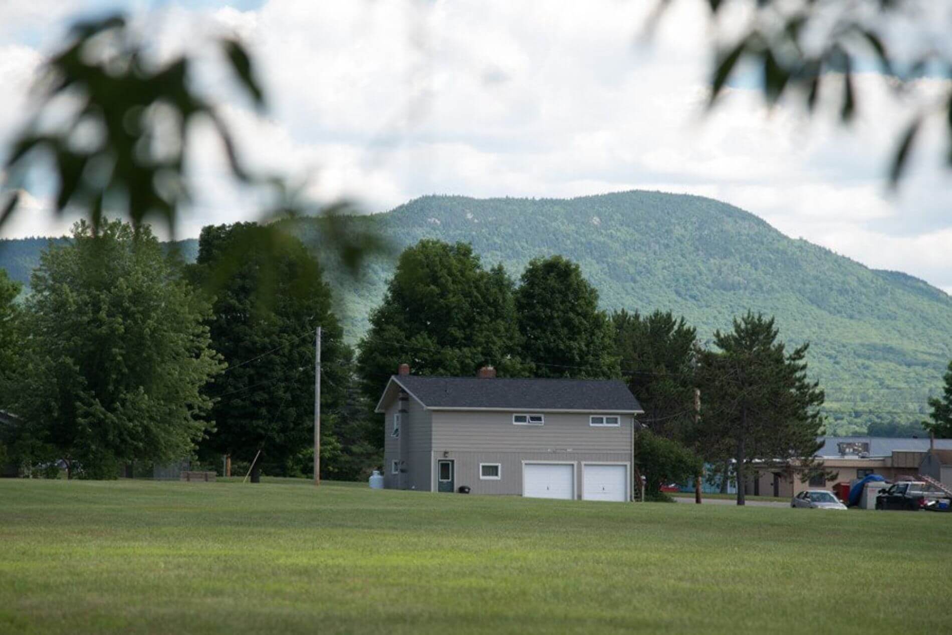 Outdoor view of two houses, one is light green with 2 car garage and parking lot.. Shows large yard.